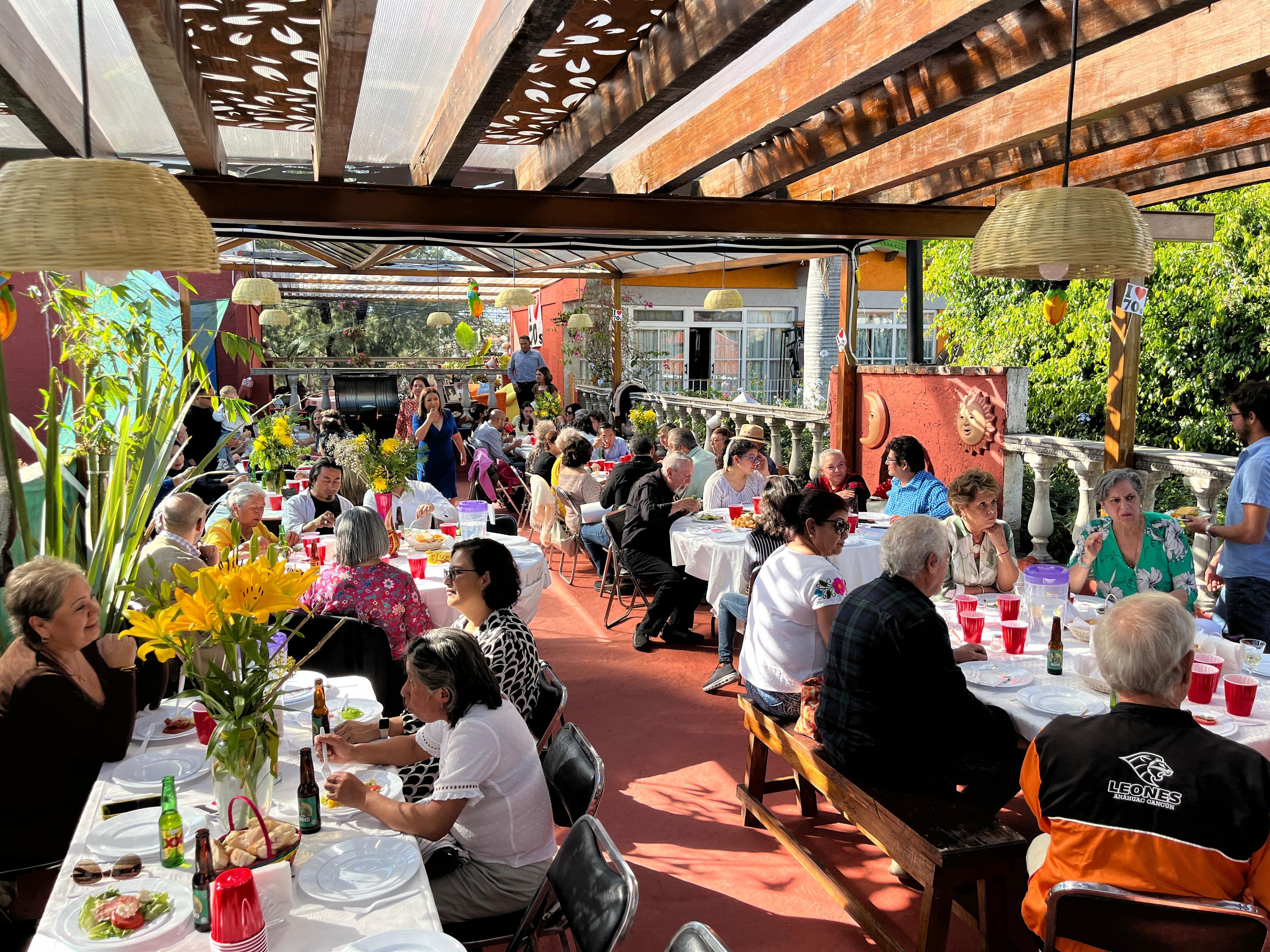 An outdoor dining area with tables and chairs, surrounded by greenery and architectural elements.