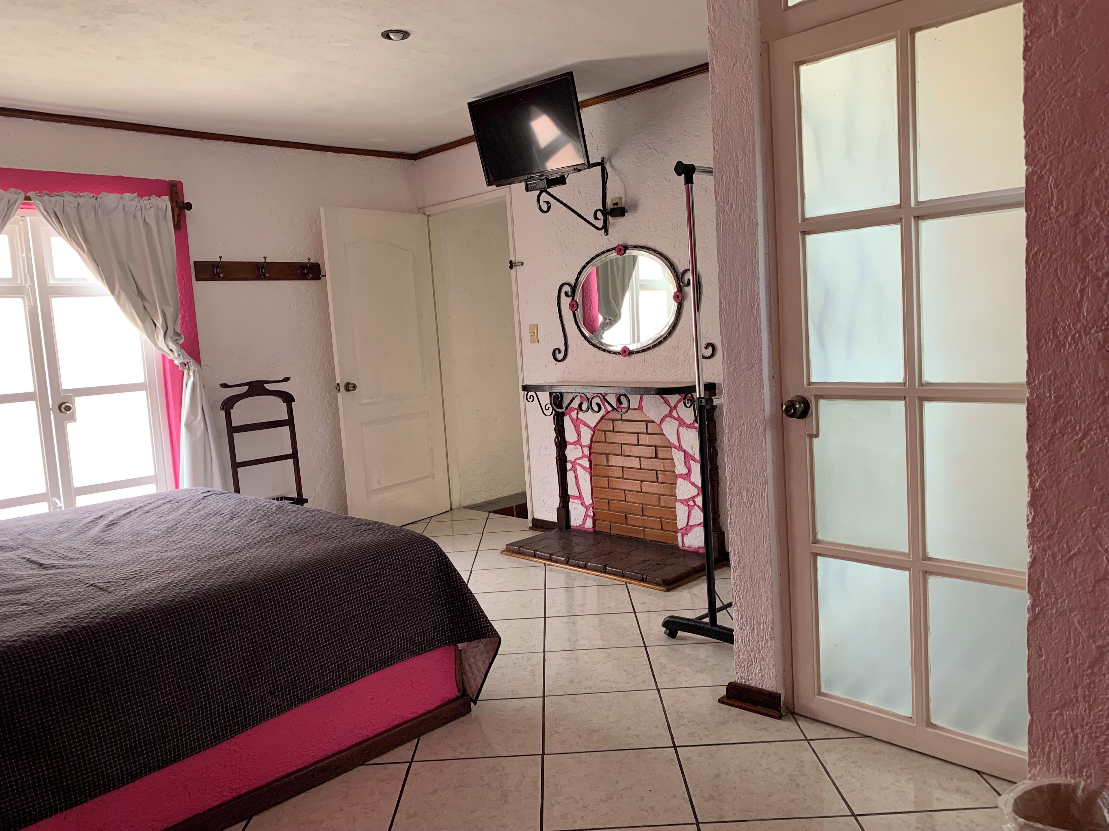 Quarto com cama, televisão na parede, espelho e lareira.