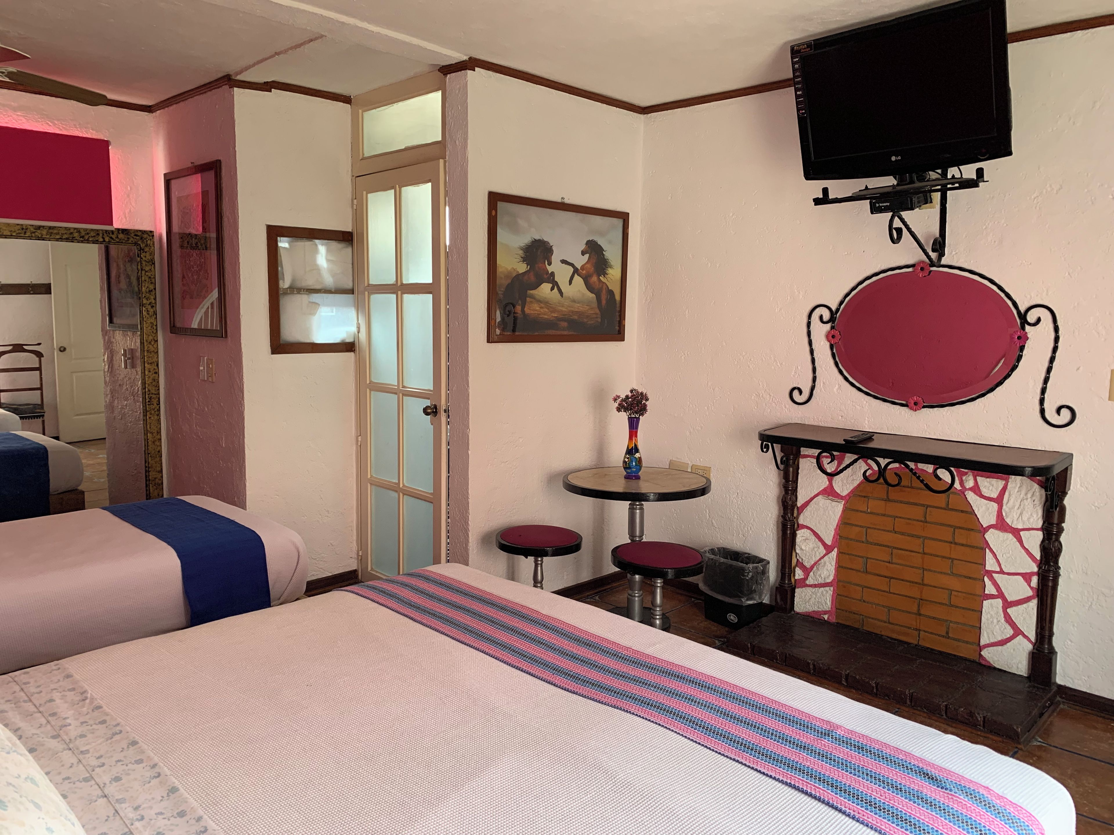 Ein Hotelzimmer mit einem Bett, einem kleinen Tisch mit einer Vase, einem Kamin und einem an der Wand montierten Fernseher.