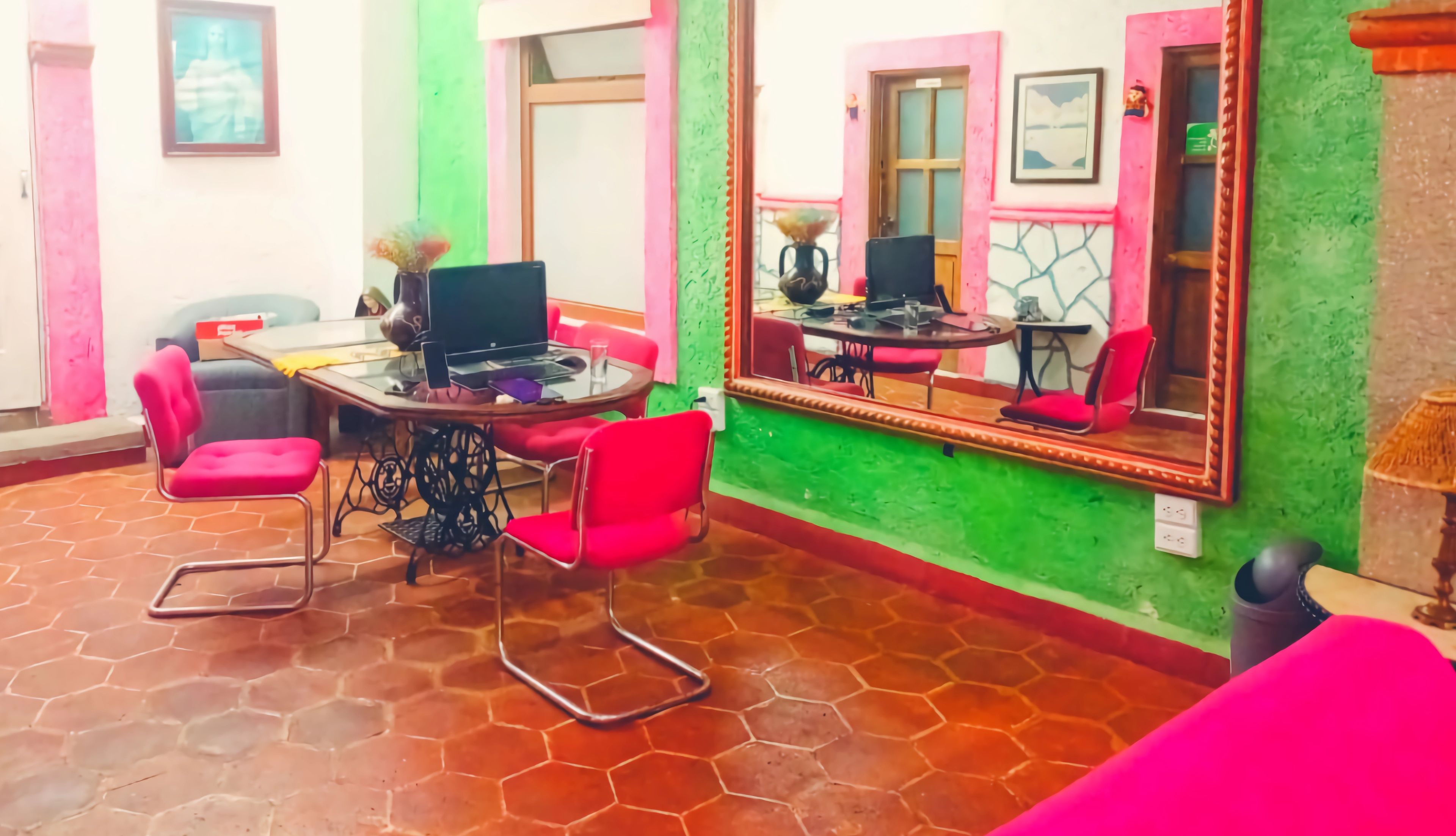 Quarto com piso de azulejos, escrivaninha com laptop, cadeiras vermelhas, espelho grande e parede de destaque verde.
