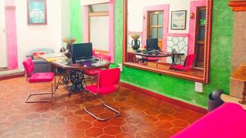 Quarto com piso de azulejos, escrivaninha com laptop, cadeiras vermelhas, espelho grande e parede de destaque verde.