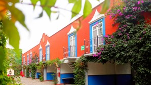 A row of colorful buildings with blue and white facades, surrounded by lush greenery and flowering plants. - Meson Yollotl (Puebla)