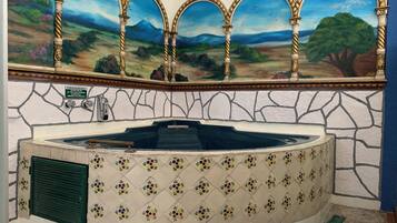 Un espace spa agrémenté d’un mur en pierre, d’un jacuzzi carrelé et d’une fresque représentant un paysage au-dessus.