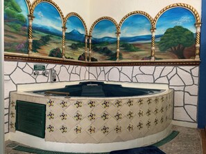 A spa area with a stone wall, a tiled jacuzzi, and a mural of a landscape above. - Meson Yollotl (Puebla)