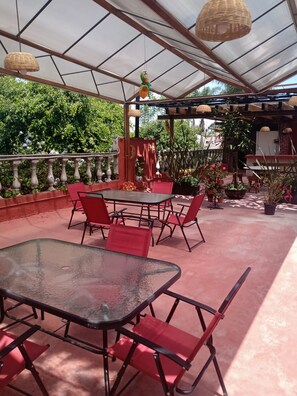 An outdoor patio with a glass table and red chairs, surrounded by potted plants and a wooden fence. - Meson Yollotl (Puebla)