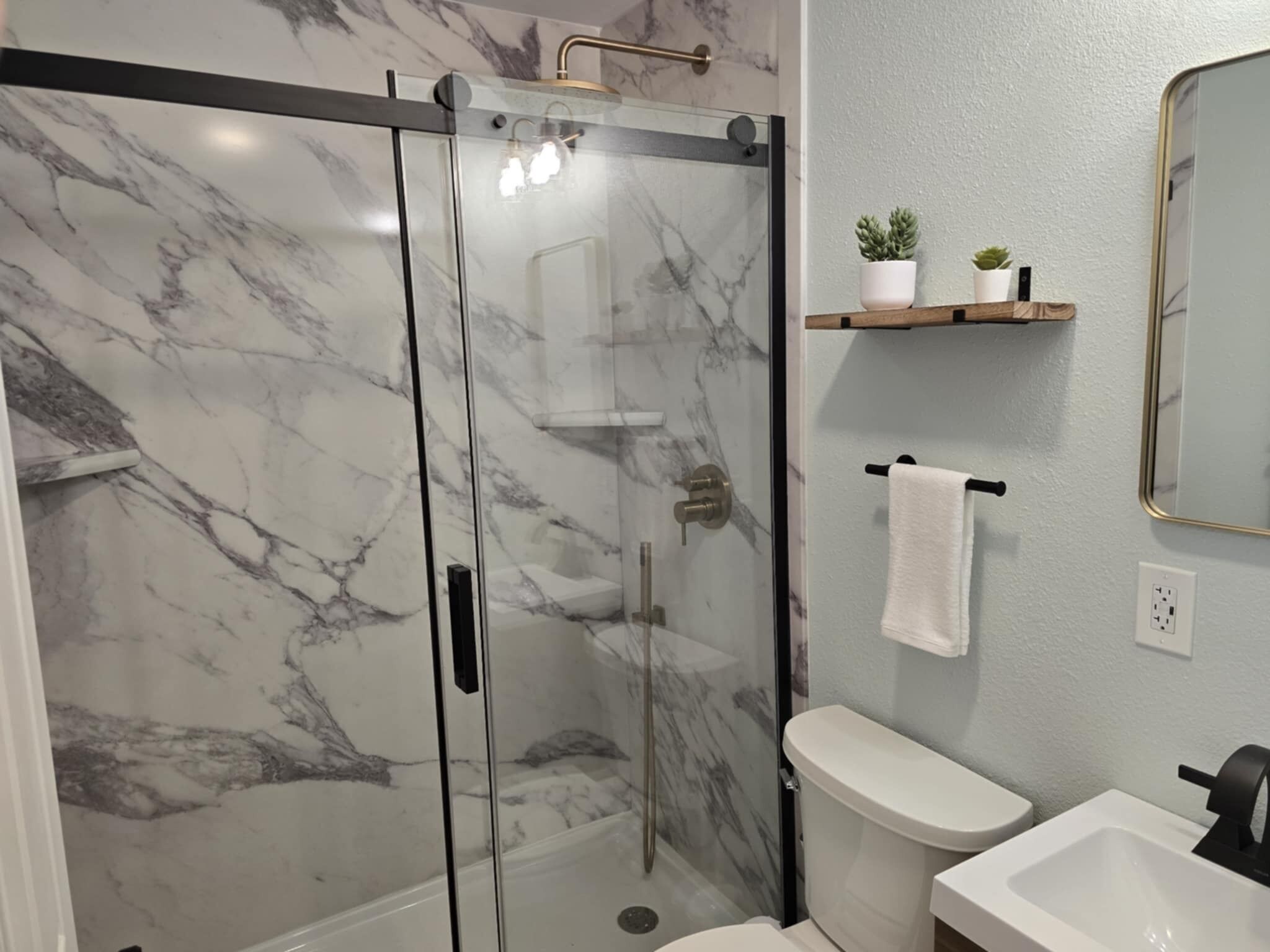 Une salle de bain avec une douche à parois de verre, des toilettes blanches, un lavabo et un miroir au mur.