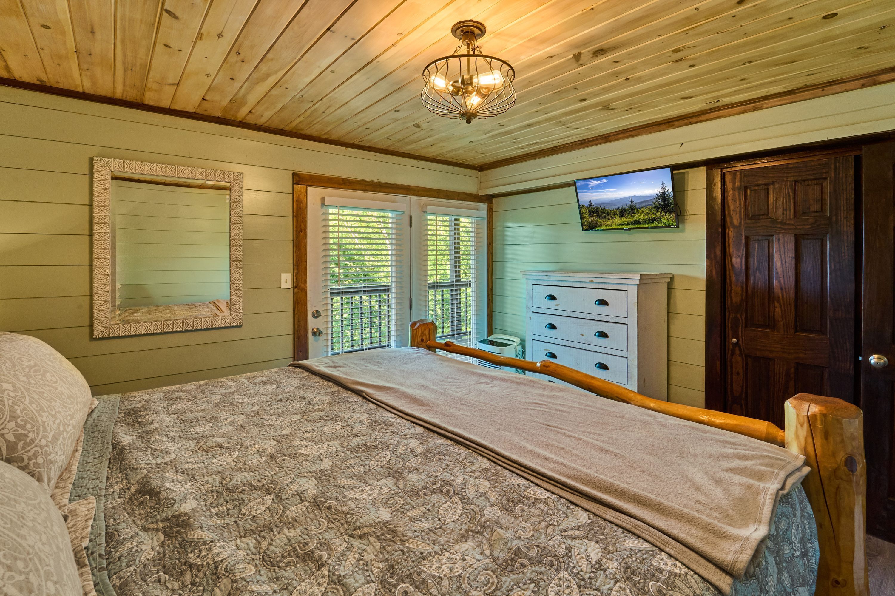 A bedroom with a bed, dresser, and a television on the wall.