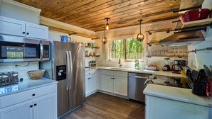 A modern kitchen with white cabinets, stainless steel appliances, and wooden ceiling beams. - Family Friendly Getaway I Hot Tub In Gatlinburg (Gatlinburg)