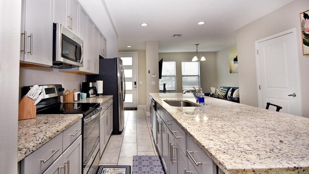 A modern kitchen with granite countertops, stainless steel appliances, and a large island with a sink. - Family place to feel at home 🏡 ! Close to everything and where you'll find it all (Kissimmee)