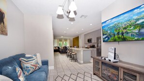 A modern living room with a blue sofa, a TV mounted on the wall, and a kitchen area with a large island. - Family place to feel at home 🏡 ! Close to everything and where you'll find it all (Kissimmee)