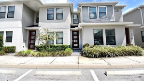 A modern multi-story residential building with a flat roof, large windows, and a well-maintained front yard. - Family place to feel at home 🏡 ! Close to everything and where you'll find it all (Kissimmee)