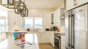 A modern kitchen with white cabinetry, a stainless steel refrigerator, and a large island with a coffee maker and a bag of chips.