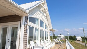 A coastal house with a deck, white exterior, and large windows.