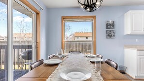 Un coin repas avec une table en bois, des assiettes blanches et des verres, le tout placé devant un mur bleu clair agrémenté d’une grande fenêtre.