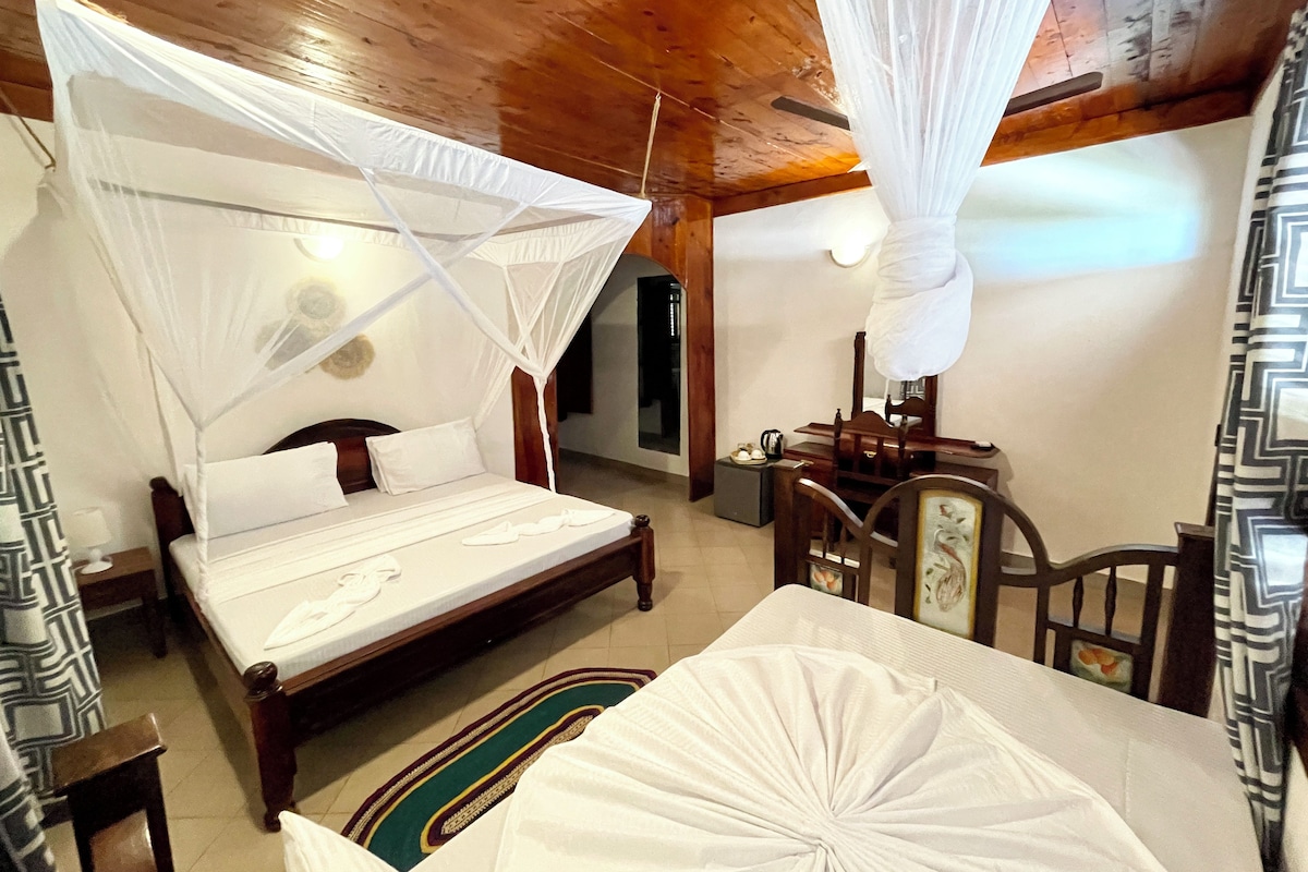 Un dormitorio con techo de madera, una cama con ropa de cama blanca, una mesita de noche, una silla y una pequeña mesa con lámpara.