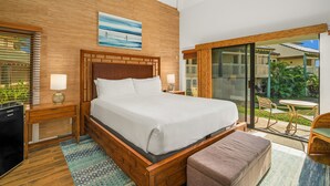 Ein modernes Hotelzimmer mit einem Holzkopfende, einem großen Bett, einem kleinen Schreibtisch, einer Bank und einer Schiebetür zu einem Außenbereich mit Tisch und Stühlen.