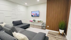 A modern living room with a sectional sofa, a flat-screen TV mounted on the wall, and a wooden accent wall.