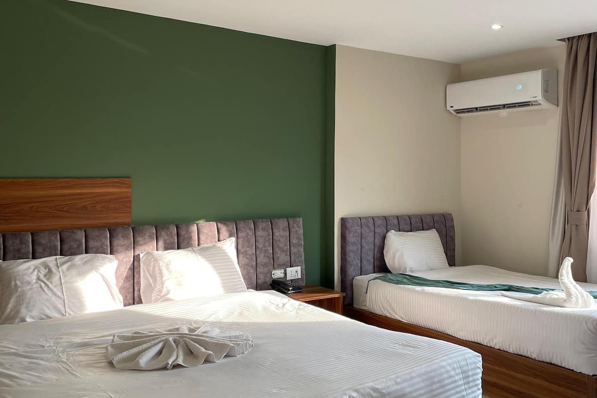 Habitación de hotel con dos camas, cabecero de madera, pared verde, unidad de aire acondicionado y una lámpara de techo roja.