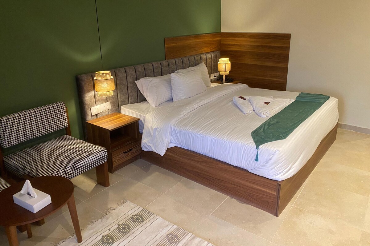 Un lit bien fait, avec du linge de lit blanc, deux lampes de chevet et un plaid vert.