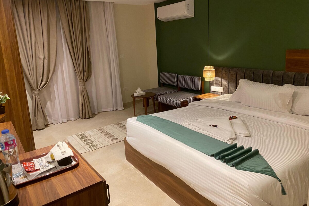 A hotel room with a bed, a desk, a chair, a lamp, and a window with curtains.