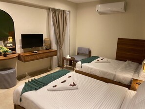 A hotel room with two beds, a TV, a desk with a lamp, and an air conditioning unit. - The Nomad Pyramids Boutique Hotel (Giza)