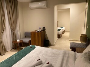 Habitación de hotel con cama, escritorio, silla, una mesita y baño visible a través de una puerta abierta.