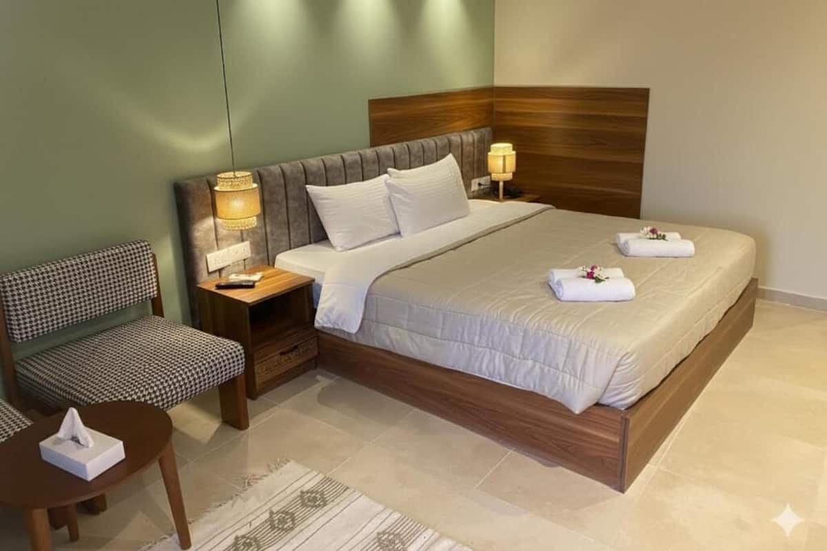 Habitación de hotel ordenada con cama, mesitas de noche, una silla y una pequeña mesa con una caja de pañuelos.