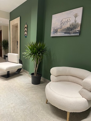 A modern living room with a green accent wall, a white armchair, a round white sofa, a potted plant, and a framed painting. - The Nomad Pyramids Boutique Hotel (Giza)