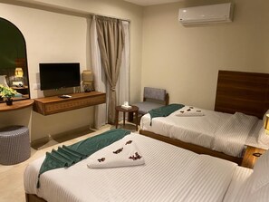 Ett hotellrum med två sängar, ett skrivbord med en platt-TV, ett litet bord och en luftkonditioneringsanläggning.