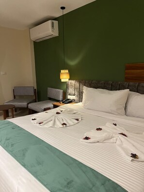 A hotel room with a bed, a chair, a bedside table, a lamp, and an air conditioning unit. - The Nomad Pyramids Boutique Hotel (Giza)