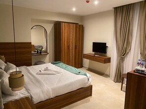 A hotel room with a bed, a TV, a wardrobe, and a desk with a mirror. - The Nomad Pyramids Boutique Hotel (Giza)