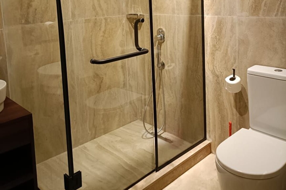 A glass-enclosed shower with a control panel, a toilet, and a marble-tiled wall.