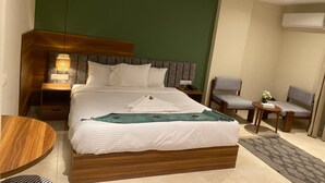 A hotel room with a bed, bedside tables, a chair, a small table, and an air conditioning unit. - The Nomad Pyramids Boutique Hotel (Giza)