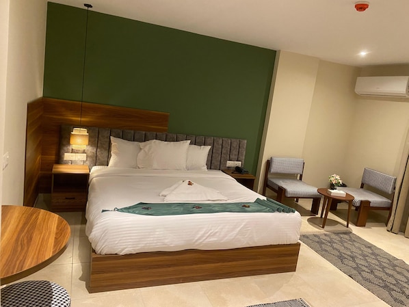 Una habitación de hotel con una cama, mesitas de noche, una silla, una pequeña mesa y un aire acondicionado.