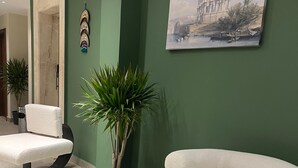 Ein modernes Wohnzimmer mit grüner Akzentwand, einem weißen Sessel, einem runden weißen Sofa, einem Topf mit Pflanze und einem gerahmten Gemälde.