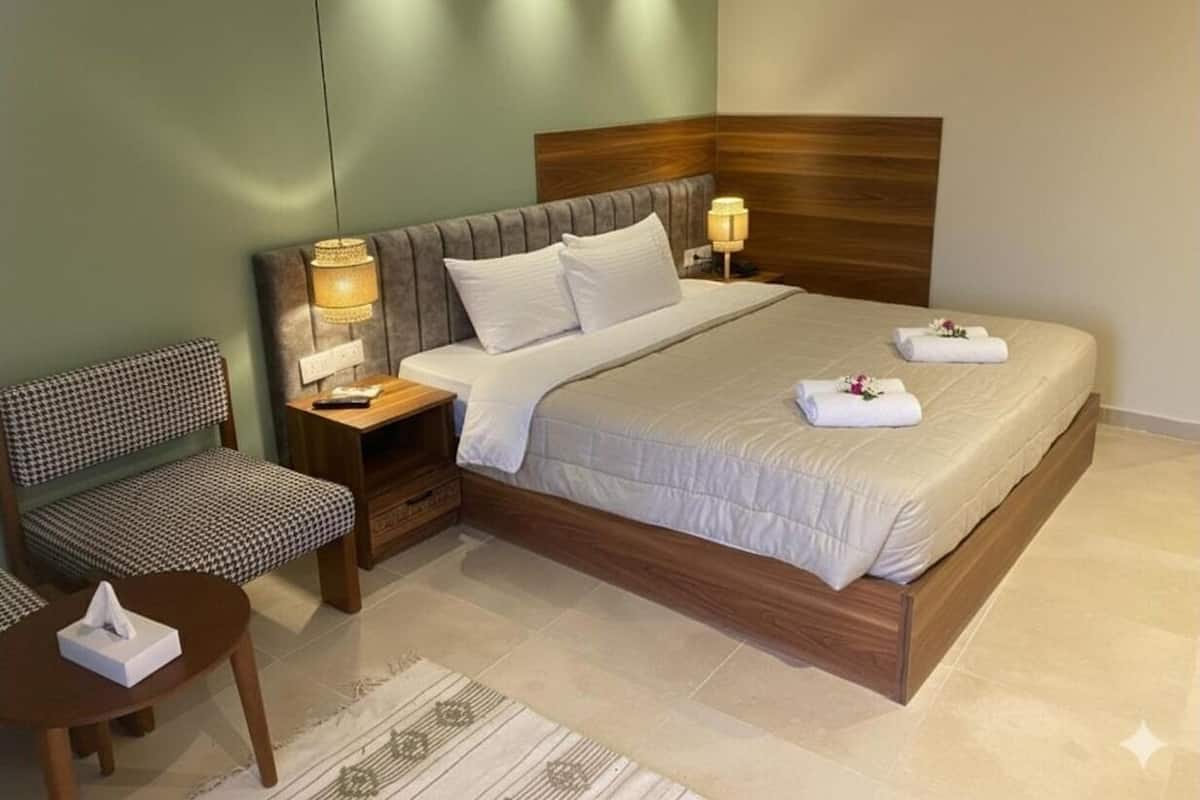 Habitación de hotel ordenada con una cama grande, una mesita de noche con lámpara, una silla y una pequeña mesa con una caja de pañuelos.