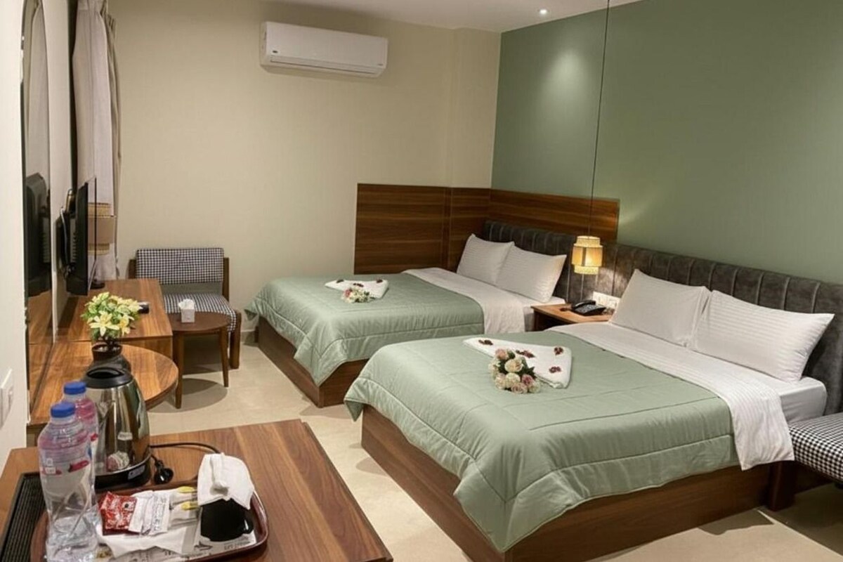 A hotel room with two beds, a desk, a chair, a TV, and an air conditioning unit.