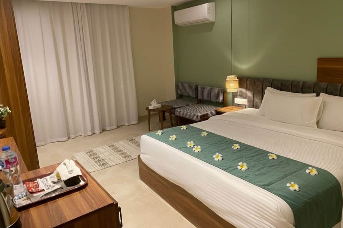 Una habitación de hotel con cama, escritorio, silla, mesita de noche, aire acondicionado y ventana con cortinas.