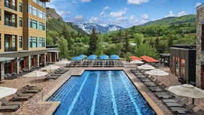 A swimming pool with lounge chairs and umbrellas, surrounded by buildings and a mountainous landscape. - Escape to the awe-inspiring beauty of Avon, Colorado and the Rockies (Avon)