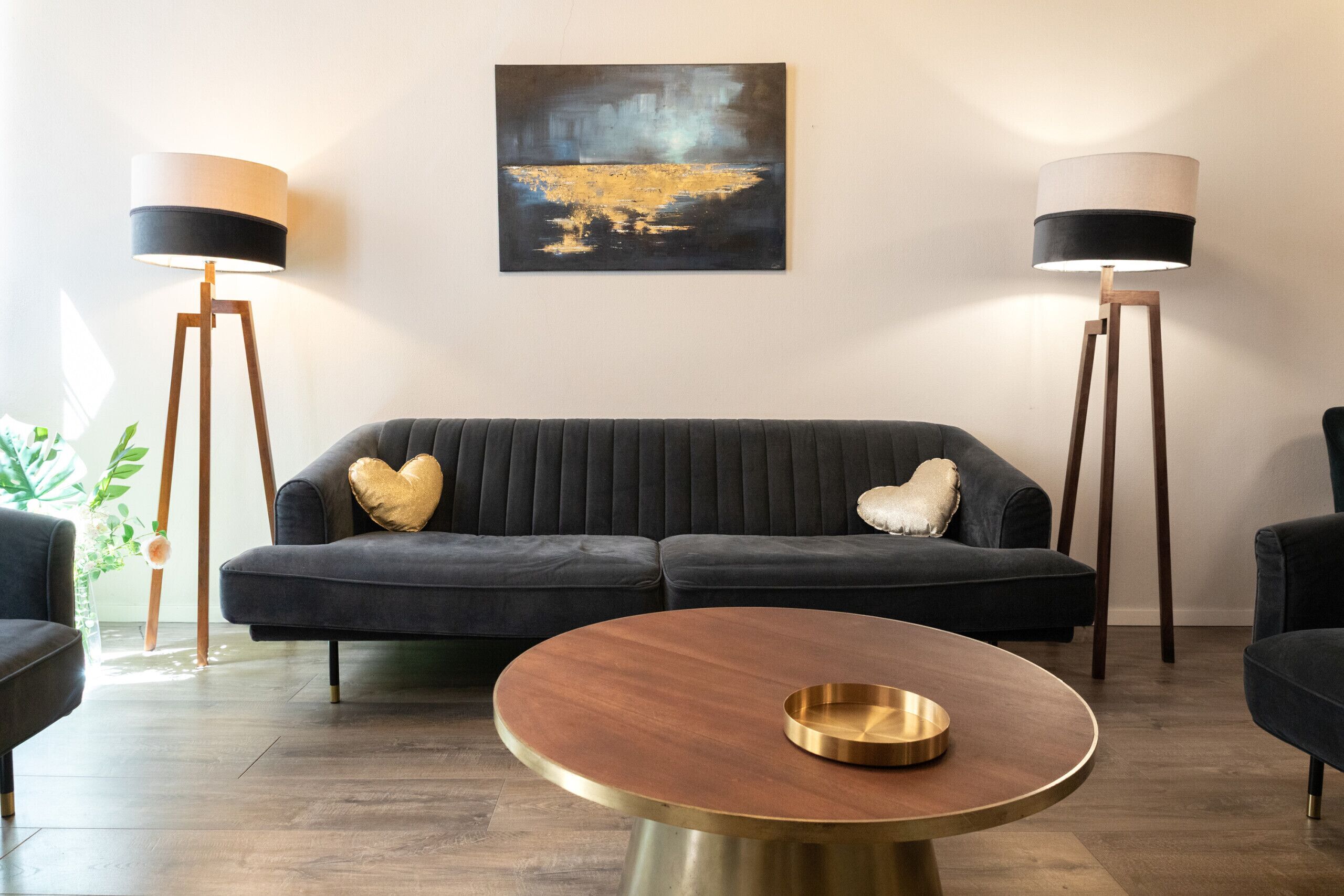 A modern living room with a dark grey sofa, two floor lamps, a round coffee table, and a painting on the wall.