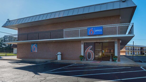 A two-story motel with a prominent '6 Office' sign, a parking lot, and a brick facade.
