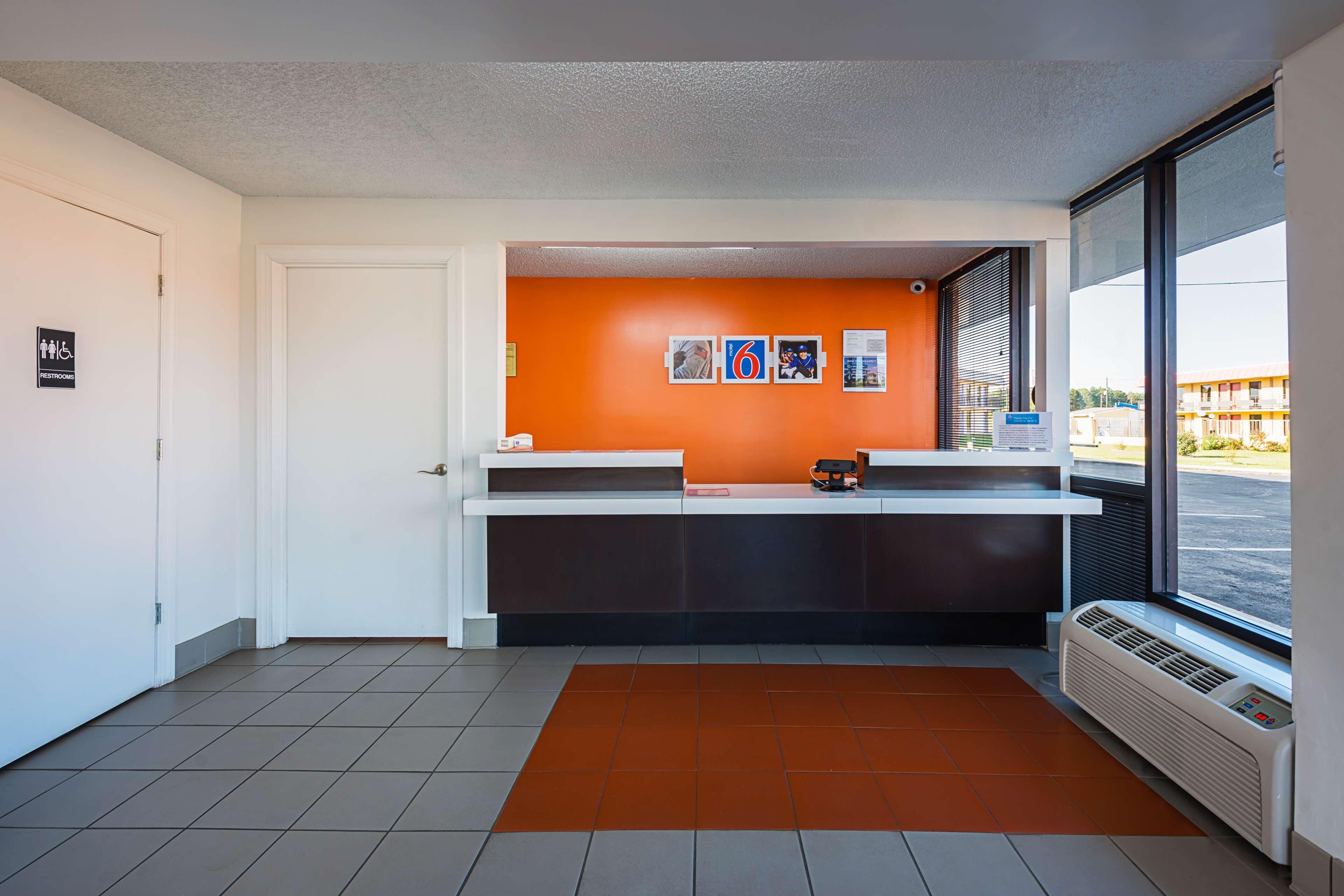 Una zona de recepción con mostrador blanco, pared naranja y vista al exterior a través de un gran ventanal.