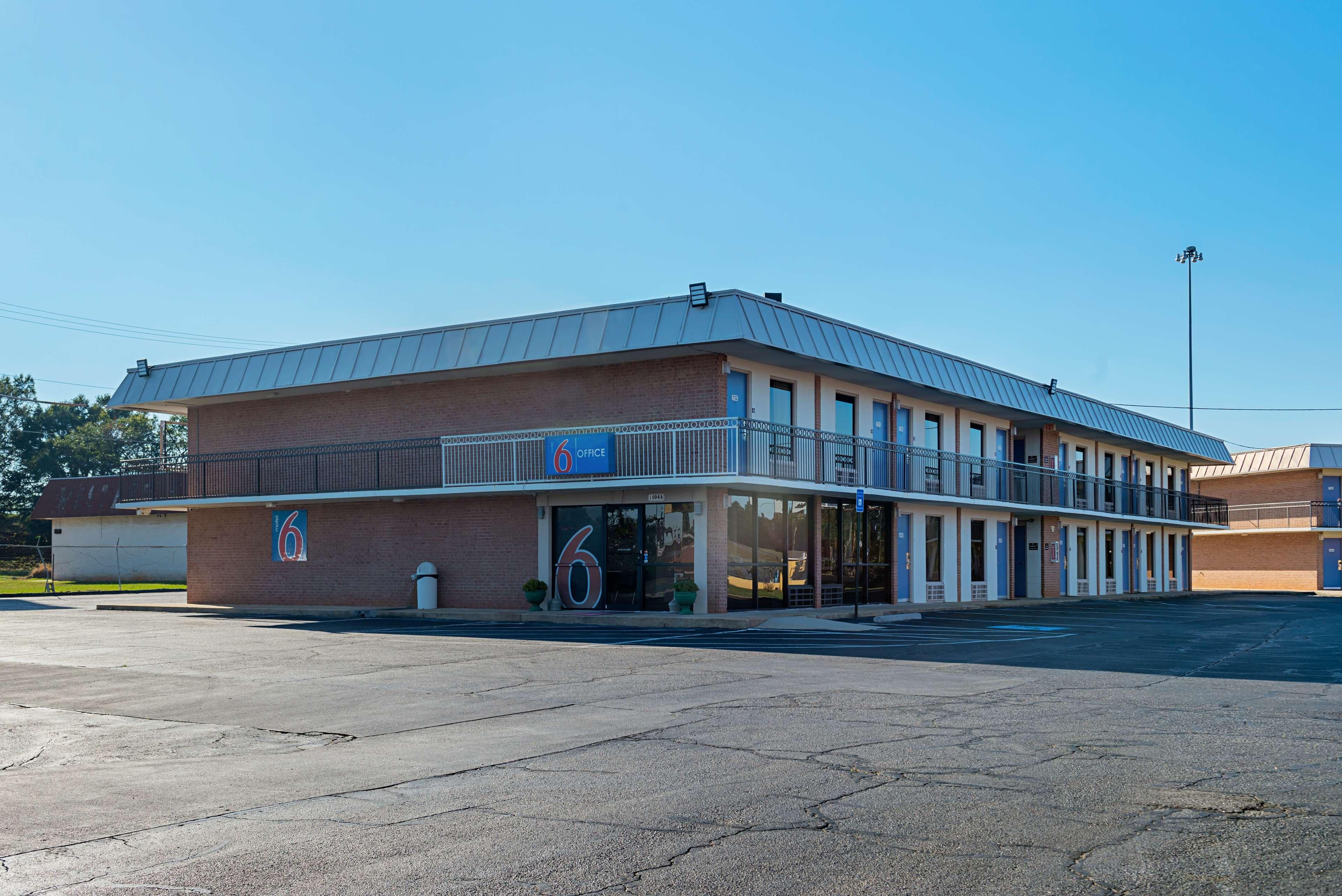 A two-story motel with a flat roof and a large parking lot in front.