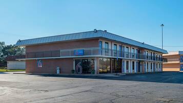 A two-story motel with a flat roof and a large parking lot in front.