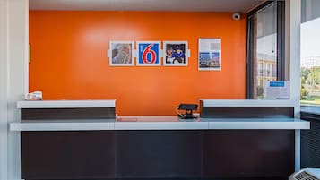 En receptionsdisk med en ljus orange vägg, en digital skärm och ett fönster med persienner.