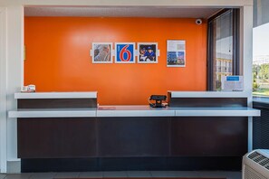 Un comptoir d’accueil avec un mur orange vif, un écran numérique et une fenêtre avec des stores.