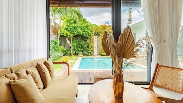 Une pièce comprenant un canapé, une table et donnant sur une piscine et un jardin.