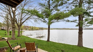 Un patio con dos sillas y una mesa con vista a un lago, con árboles y un muelle al fondo.