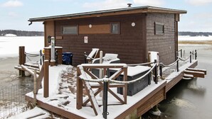 Una cabaña de madera con una pequeña terraza, un jacuzzi y una sauna.