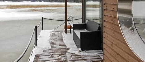 En træterrasse med et glasindhegning, et polstret siddeområde og udsigt til et snelandskab.
